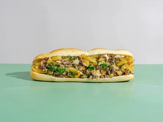 Algerian baguette sandwich filled with fries, omelette, herbs and additional garnish.